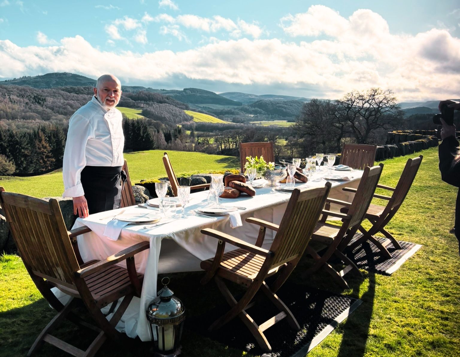 Private chef in Scotland — Giuseppe Manzoli setting a long table for an Italian-inspired dinner with a Scottish hillside behind