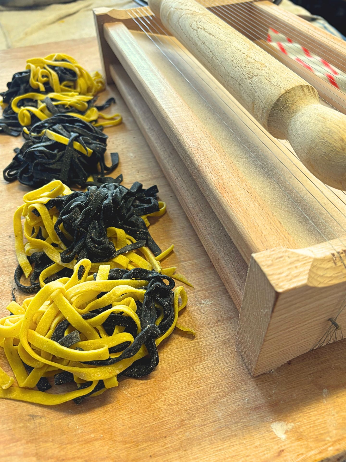 Giuseppe Manzoli hand-cutting fresh pasta — yellow egg tagliatelle and black squid-ink pasta on a traditional Italian chitarra