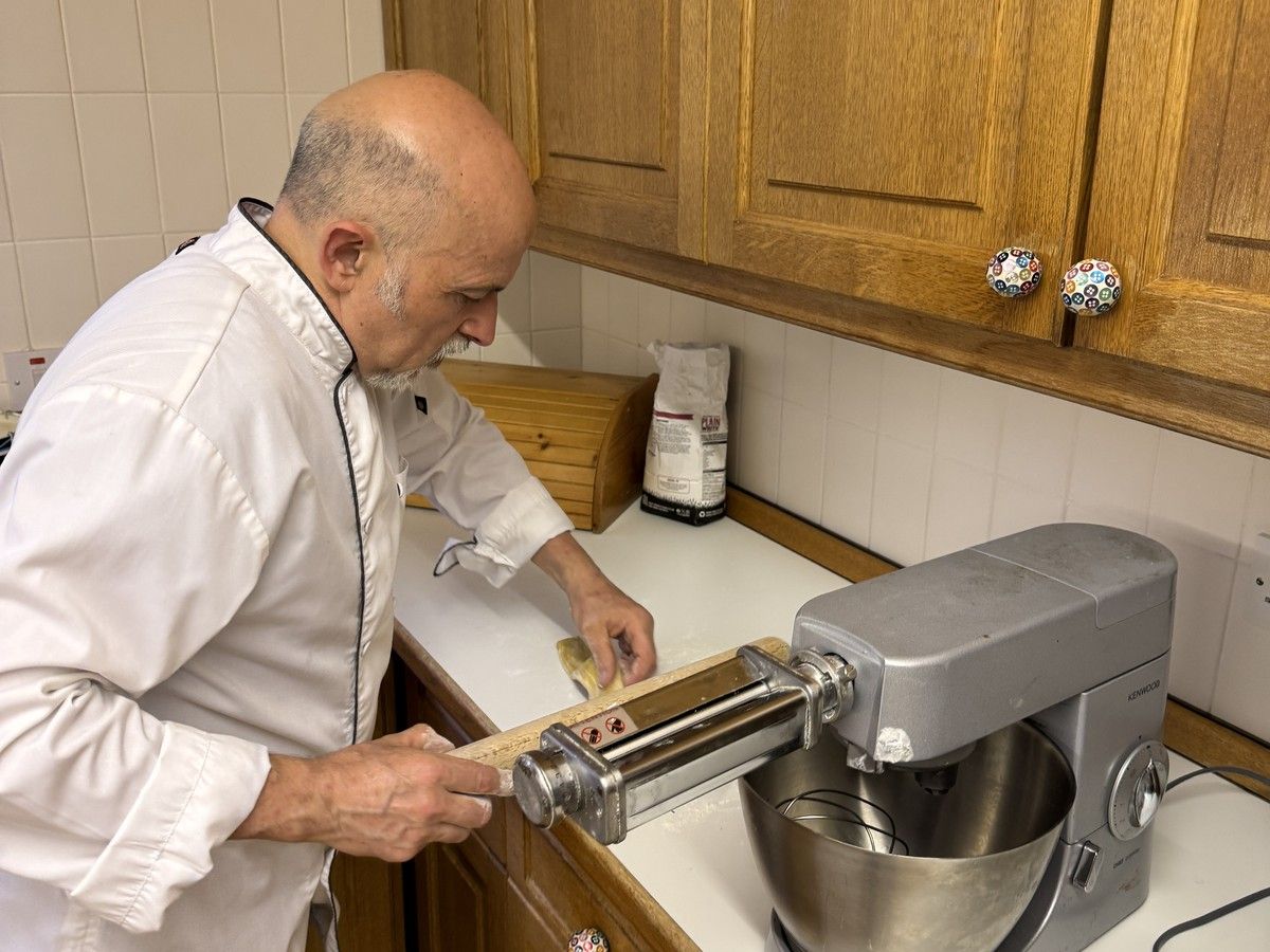 Italian private chef rolling fresh pasta dough through a pasta machine in a country house kitchen near Stirling, Scotland