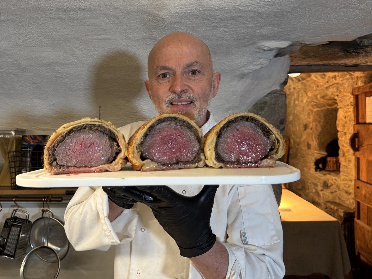 Italian private chef holding a board of sliced beef Wellington cooked pink, in the stone-walled kitchen at Kilmartin Castle, Argyll
